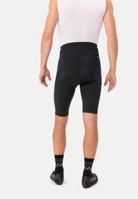 Fekete kerékpáros short magas derékkal, párnázott ülőrésszel és matt felszíni textúrával. Fekete zoknikkal párosítva, geometrikus mintával és elegáns cipőkkel.