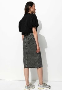 Haut noir à manches bouffantes coupé avec un ourlet festonné, associé à une jupe en denim grise taille haute arrivant au genou. Le modèle porte des baskets argentées.