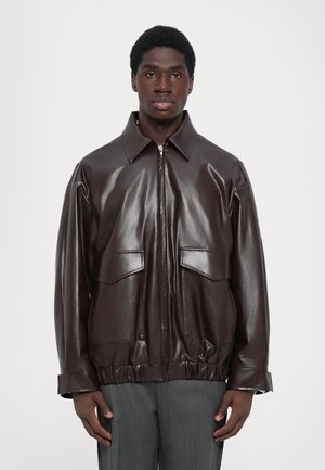 Veste en cuir marron avec fermeture éclair à l'avant, grandes poches poitrine et ourlet froncé. Dispose d'un col classique et d'une texture lisse et brillante.
