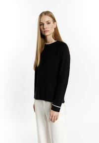 Schwarzer Strickpullover mit rundem Halsausschnitt und weißem Besatz am Halsausschnitt und an den Bündchen, mit lockerer Passform und langen Ärmeln.