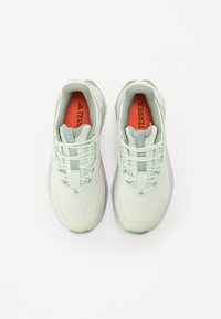 Helles grünes Sportschuhmodell mit einem Obermaterial aus Textil, Mesh-Akzenten und einer gepolsterten Sohle. Verfügt über eine Schnürverschluss und orangen Branding der Einlegesohle.