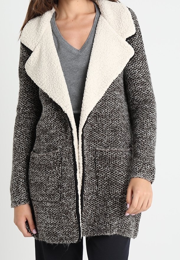 Stickad cardigan med ett strukturerat grått och svart mönster, kontrasterande krämfärgad fuskpäls-krage och framfickor. Öppen framdesign.