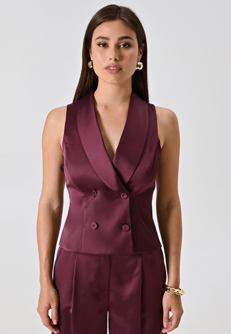 Top doppiopetto in raso borgogna con ampi risvolti e due bottoni, caratterizzato da un design aderente e senza maniche. Texture liscia.