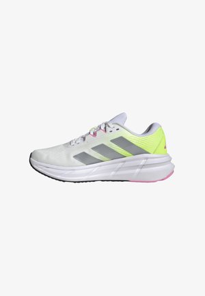 Zapatillas deportivas blancas con rayas grises, acentos en amarillo neón y una parte superior de malla texturizada. Cuenta con una entresuela blanca gruesa y una suela negra.