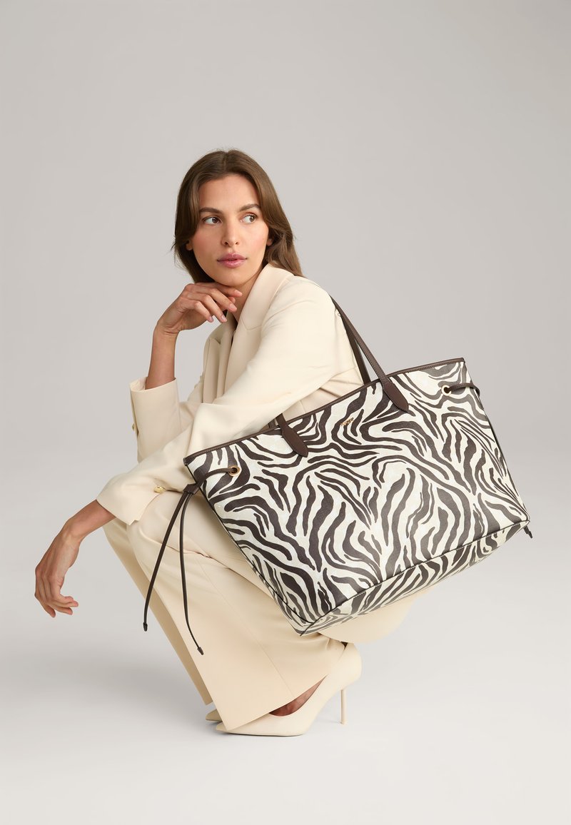 Sac fourre-tout à motifs zèbre en noir et blanc, avec des poignées en cuir marron, un design spacieux et une finition texturée.