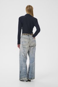 Marineblauw shirt met lange mouwen gecombineerd met lichte, versleten wijdvallende jeans met een bruine riem met metalen accenten, gezien van achteren.