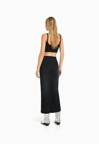 Conjunto de top corto negro y falda larga con cintura ajustada. La modelo lleva botas plateadas hasta la rodilla. Textura suave y diseño minimalista.
