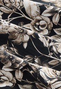 Juoda medžiaga su sudėtingais gėlių raštais smėlio spalvos bei rudos spalvos atspalviais, su detaliais lapais ir žiedais, sukurianti tekstūruotą išvaizdą.