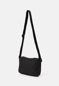 Kleine zwarte stoffen crossbody tas met verstelbare schouderband en ritsluiting, afgebeeld tegen een witte achtergrond.