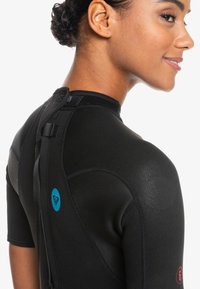 Combinaison de plongée noire à manches courtes avec une texture lisse, arborant un logo de cœur bleu et un détail numérique rouge au dos, fermeture à sangle ajustable.