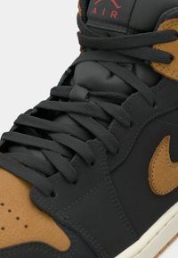 Črne in rjave Nike Air tenisice z teksturirano zgornjim delom, debelimi vezalkami, perforiranim prstom in značilnim logotipom.