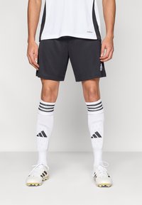 Crne sportske kratke hlače, bijele čarape do koljena s prugama i bijele nogometne kopačke sa žutim šiljcima. Jednostavan dizajn s vidljivim detaljima marke.