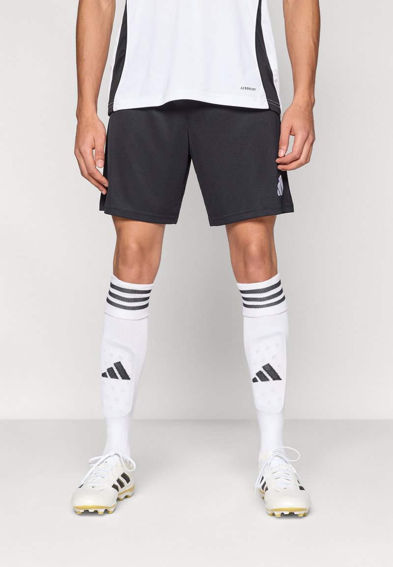 Crne sportske kratke hlače, bijele čarape do koljena s prugama i bijele nogometne kopačke sa žutim šiljcima. Jednostavan dizajn s vidljivim detaljima marke.