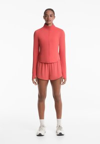 Rode sportset bestaande uit een aansluitende lange mouw zip-up top en shorts. Glad, rekbaar materiaal met een hoge kraag en een elastische tailleband.