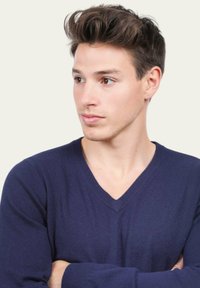 Pull marin à col en V avec manches longues, fabriqué dans un matériau en tricot lisse. Le modèle a les bras croisés et se tourne légèrement sur le côté.