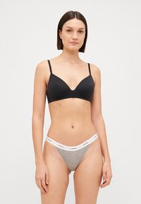 Soutien-gorge rembourré noir avec bretelles réglables associé à un string gris clair arborant une ceinture avec logo blanche, en matériaux lisses et avec un design minimaliste.