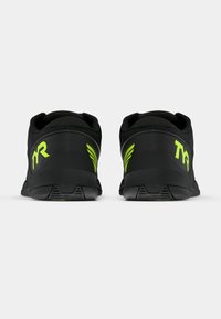 Zapatillas deportivas negras con parte superior de malla, con llamativos acentos verdes en el talón y en la marca, y una suela de goma texturizada.