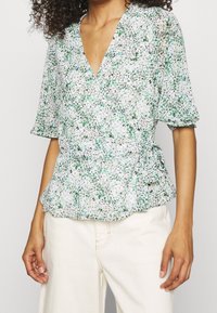 Top avvolgente floreale verde e bianco con maniche corte, scollo a V e vita arricciata. Tessuto leggero con una finitura testurizzata.