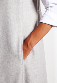 Grå filtklänning med en mjuk struktur, försedd med en sidficka och en vit långärmad skjorta under. Enkelt, minimalt utseende.