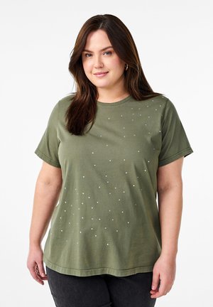 Olivinės spalvos medvilninis T-shirts su trumpomis rankovėmis, apvaliu kaklu ir išbarstytais sidabriniais kalnų kristalais priekyje, derinamas su tamsiomis džinsomis.