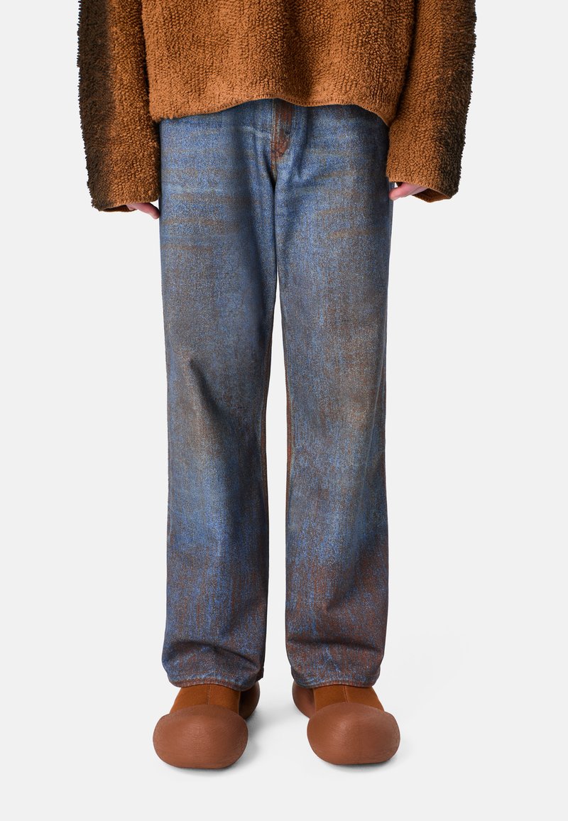 Pantaloni in denim a motivi blu e marrone con una vestibilità rilassata, abbinati a scarpe rotonde marroni e a un maglione marrone texture.