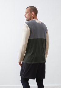 Langsleeve sportshirt met een kleurblokontwerp met grijze, crèmekleurige en donkergroene panelen; lichtgewicht, gladde textuur en minimale stiksels.