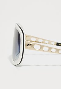 Occhiali da sole con montatura bianca, dettagli neri e ampi lenti oscurati. Le aste in metallo dorato presentano un motivo a intaglio e un dettaglio del logo.