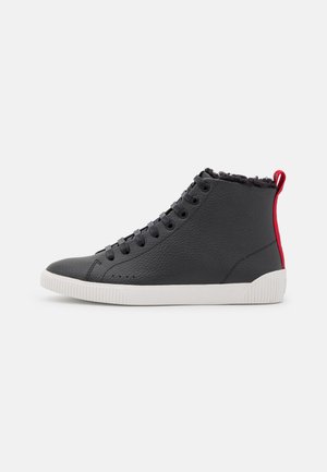 Zapatillas altas de cuero negro con acabado texturizado, suela de goma blanca y acento rojo en la parte trasera; parte delantera con cordones y ojales.