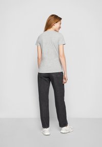 T-shirt grigio a maniche corte con scollatura rotonda, abbinato a pantaloni in denim scuro. La schiena del modello è rivolta verso la fotocamera, in piedi contro uno sfondo neutro.