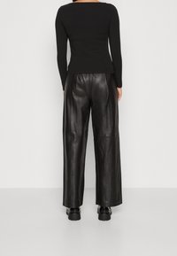 Musta pitkähihaisen yläosa yhdistettynä korkeavyötäröisiin mustiin leveälahkeisiin nahkahousuihin. Sileä pinta, minimalistinen muotoilu ja hienovaraiset tikkausyksityiskohdat näkyvissä.