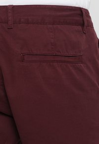Burgundy pamut nadrág sima textúrával, hátsó zsebbel és övcsat loopokkal. Az anyag enyhe fényt jelenít meg, és testre szabott illeszkedést biztosít.