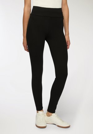 Leggings neri con vita alta, realizzati in tessuto elasticizzato, caratterizzati da una texture liscia e un design aderente, abbinati a sneakers bianche.