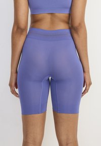 Fioletowe sportowe spodenki wykonane z elastycznego materiału, z wysokim stanem i widocznymi detalami szwów, zaprojektowane z myślą o komforcie i swobodzie ruchów.