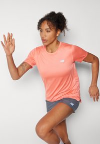 Sportlik riietus, mis sisaldab eredat koralli värvi lühikeste varrukatega särki ja halli lühikestesse pükstes, mõlemad koos New Balance'i logodega. Sile tekstuur, parajalt keha ligi.
