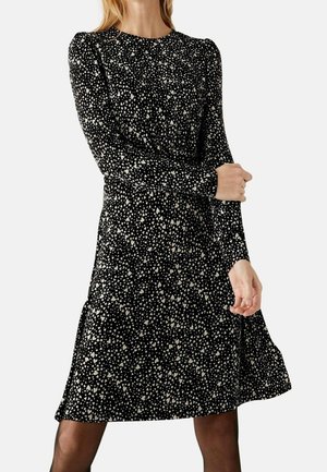 Robe noire à manches longues avec un motif de petits cœurs blancs éparpillés, encolure ronde et jupe fluide. Tissu doux avec une légère élasticité.