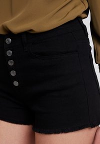 Pantalones cortos de mezclilla negros con un dobladillo deshilachado y cinco botones metálicos. Presentan bolsillos laterales y un diseño ajustado para un aspecto aerodinámico.