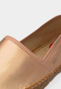 Κοντινό πλάνο μεταλλικού ροζ χρυσού παπουτσιού slip-on με υφή στη σόλα και χαραγμένη τη λέξη "LOVE" στο πλάι.