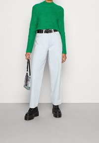 Zielony sweter z dzianiny, jasnoniebieskie dżinsy z wysokim stanem, czarny pasek z ćwiekami i botki na platformie. W ręku trzymana mała torebka w wzorki.