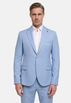 Man wearing light blue suit with white dress shirt, standing against plain light background, facing forward with neutral expression.