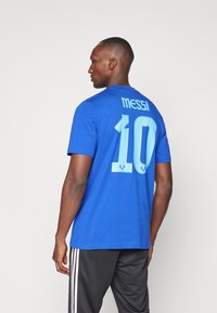 Blaues Baumwoll-T-Shirt mit kurzen Ärmeln. Auf der Rückseite steht "MESSI" in hellblauer Schrift und darunter die Zahl "10" in größerer hellblauer Schrift.