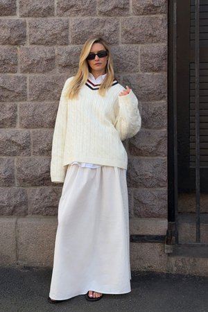 Krämfärgad kabelstickad tröja med svart och röd v-ringning, över en vit blus, i kombination med en flödande vit maxikjol och platta sandaler.
