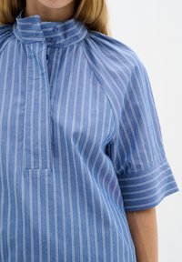 Blå randig skjorta i lättviktig tyg. Har en hög krage, knappstängning och korta ärmar med en avslappnad passform.