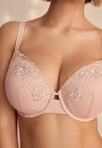 Bra rosa chiaro con ricami floreali, supporto con stecche e spalline regolabili. Presenta una chiusura a gancio e occhiello sul retro.