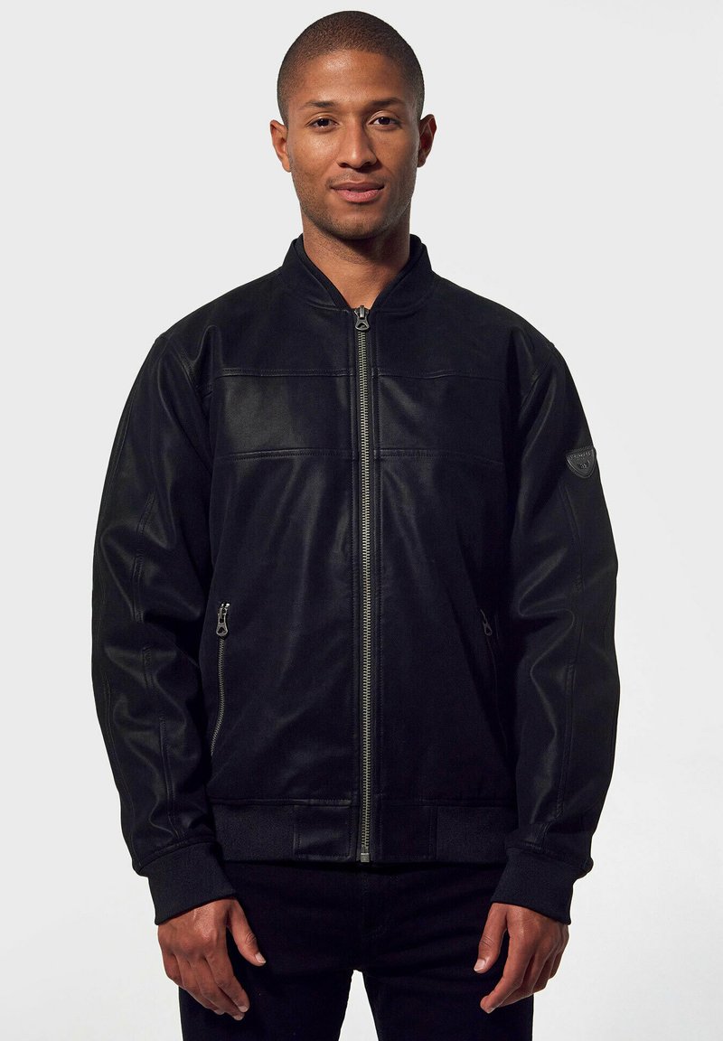 Giacca bomber nera in pelle con zip frontale, due tasche laterali e polsini a costine. Presenta un design semplice senza motivi visibili.