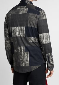 Chemise à manches longues pour hommes en gris et bleu foncé avec un design patchwork géométrique. Fabriquée en tissu doux avec des poignets boutonnés et un col pointu.