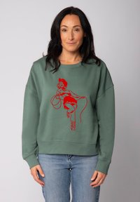 Grüner Pullover mit einem roten Grafikdruck einer Frau, die einen Lasso hält. Hat eine lockere Passform, Rundhalsausschnitt und Rippbündchen.