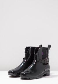 Botas de lluvia negras de goma brillante; diseño de altura hasta el tobillo, suela texturizada, paneles laterales elásticos y detalle de hebilla decorativa.