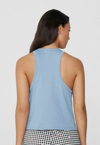 Top sin mangas de color azul claro, hecho de una tela suave, con un escote redondo y un diseño de espalda tipo corredor. Textura sencilla, sin patrones visibles.