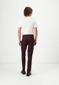 Burgundy maßgeschneiderte Hose mit Slim-Fit, flachem Vorderteil, Gürtelschlaufen und einer Gesäßtasche, kombiniert mit einem weißen Kurzarmhemd.