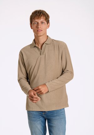 Polo a maniche lunghe a coste in beige, con colletto e vestibilità rilassata, abbinato a jeans blu per un look casual.